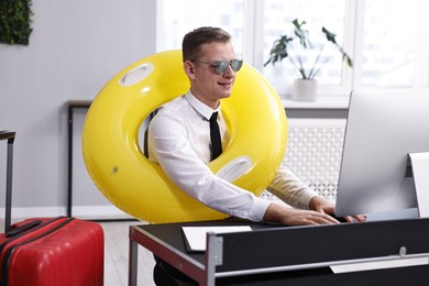 Photo of Businessman with inflatable ring and sunglasses at workplace in office