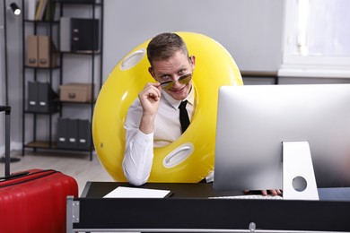 Photo of Businessman with inflatable ring and sunglasses at workplace in office