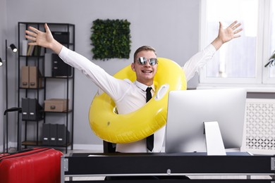 Photo of Businessman with inflatable ring and sunglasses at workplace in office