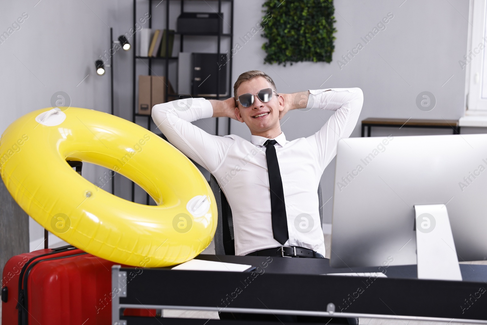 Photo of Businessman with inflatable ring and sunglasses at workplace in office