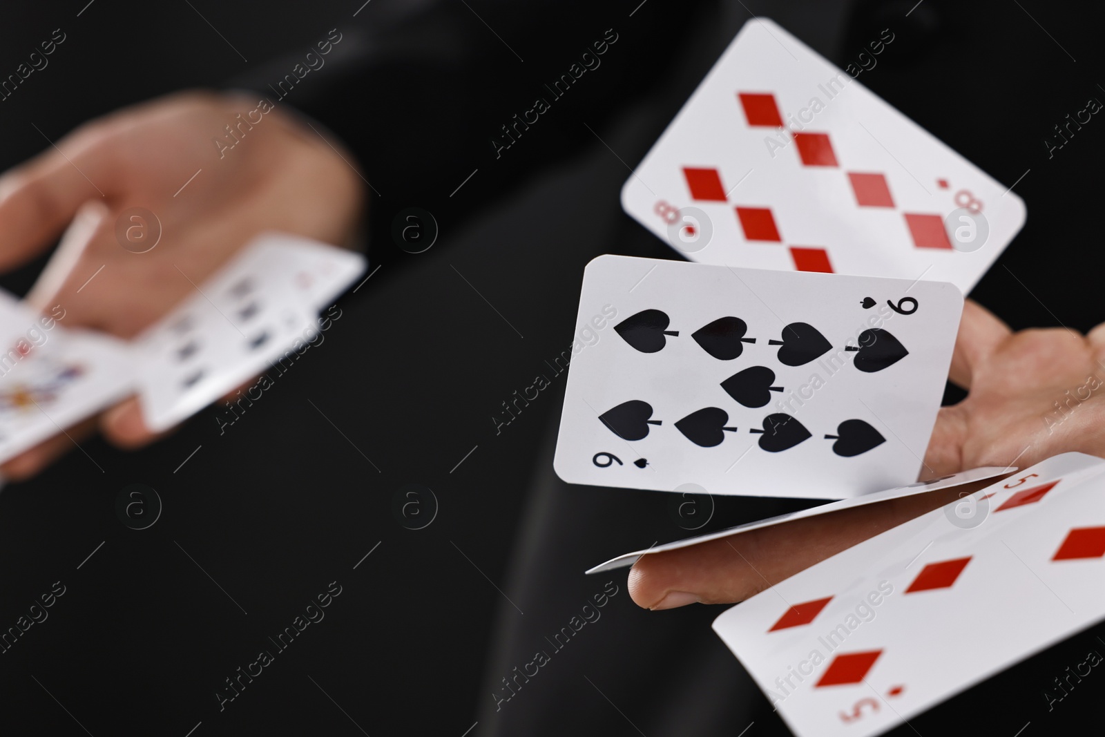 Photo of Illusionist showing trick with playing cards on black background, closeup