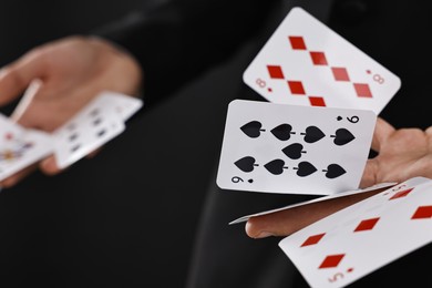 Illusionist showing trick with playing cards on black background, closeup