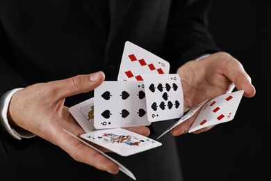 Photo of Illusionist showing trick with playing cards on black background, closeup