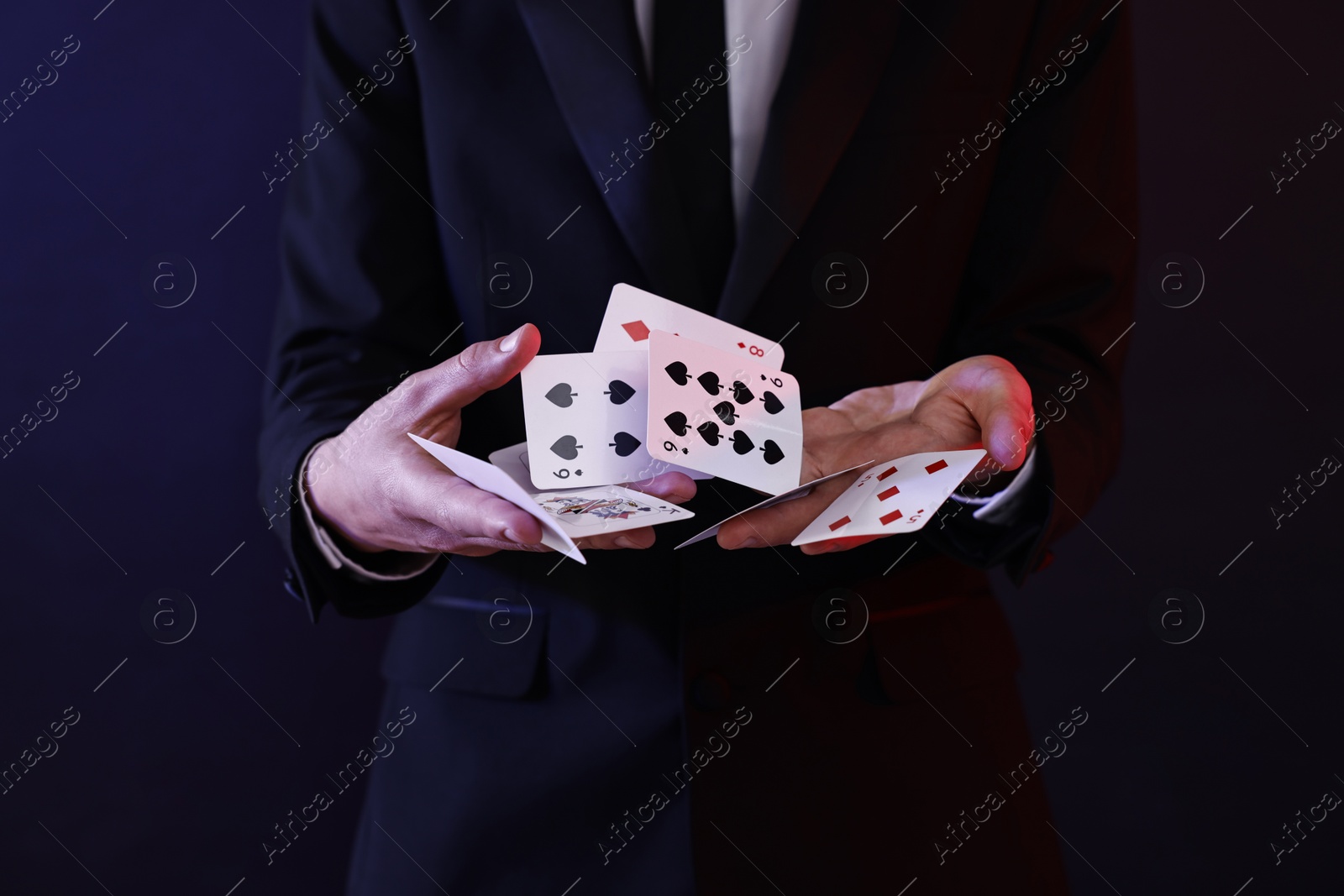 Photo of Illusionist showing trick with playing cards on dark background, closeup