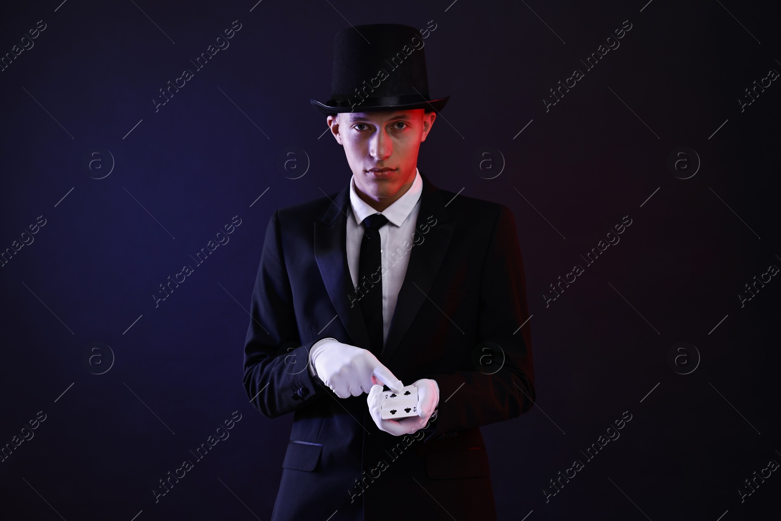 Photo of Illusionist showing trick with playing cards on dark background