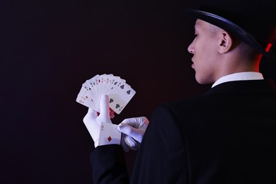 Photo of Illusionist hiding one playing card up his sleeve while showing deck on dark background, space for text