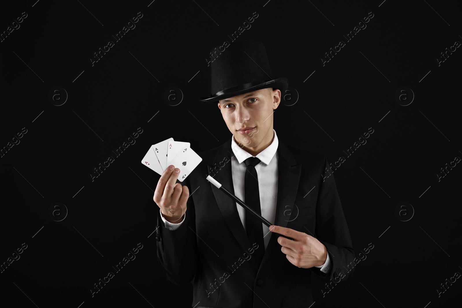 Photo of Illusionist pointing magic wand on playing cards against black background