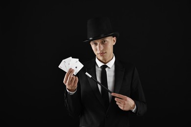 Illusionist pointing magic wand on playing cards against black background