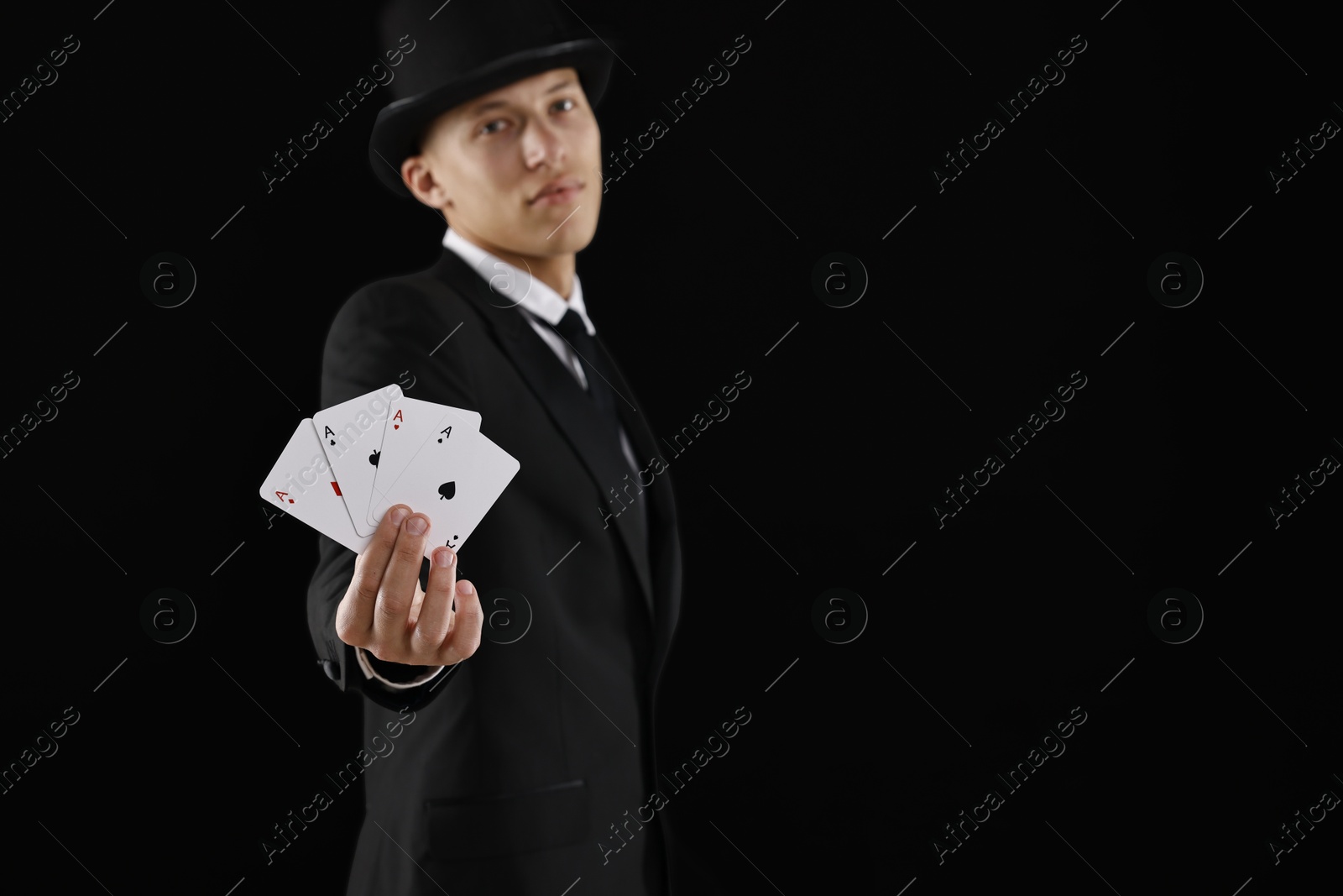 Photo of Illusionist showing playing cards on black background, selective focus. Space for text