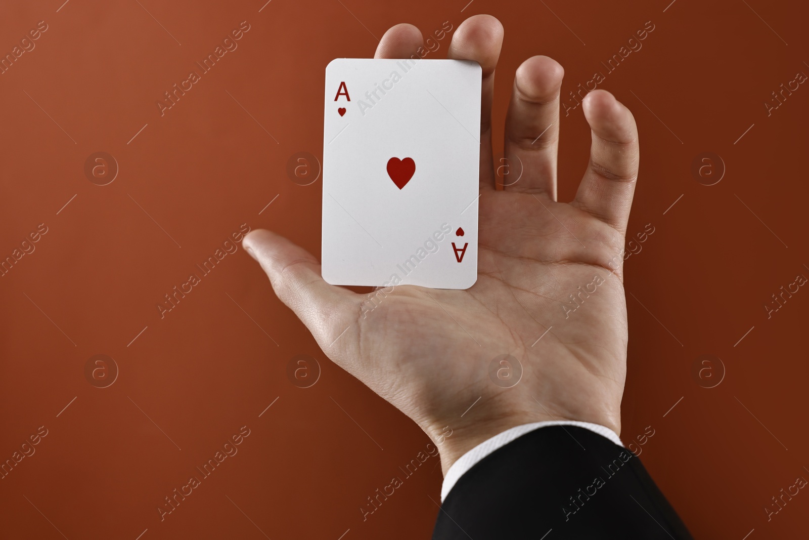 Photo of Illusionist showing playing card on dark orange background, closeup. Space for text