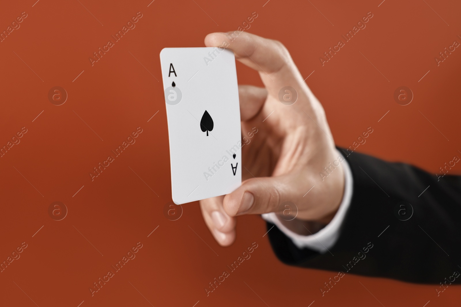 Photo of Illusionist showing playing card on dark orange background, closeup. Space for text