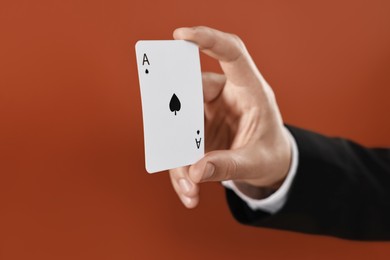 Photo of Illusionist showing playing card on dark orange background, closeup. Space for text