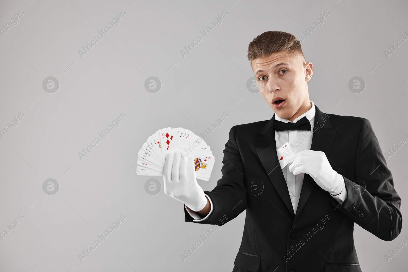 Photo of Illusionist hiding one playing card behind jacket lapel while showing deck on grey background, space for text