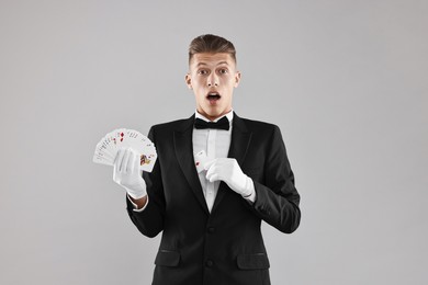 Photo of Illusionist hiding one playing card behind jacket lapel while showing deck on grey background