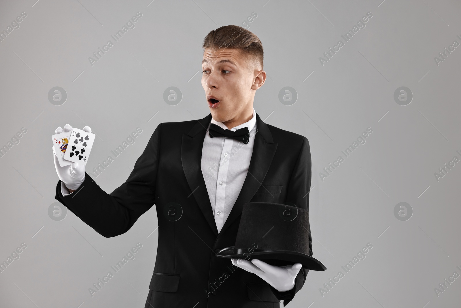 Photo of Illusionist with top hat showing playing cards on grey background