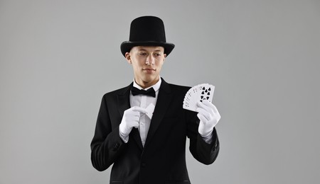 Photo of Illusionist hiding one playing card behind jacket lapel while showing deck on grey background