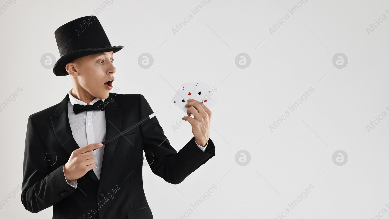 Photo of Illusionist pointing magic wand on playing cards against white background. Space for text