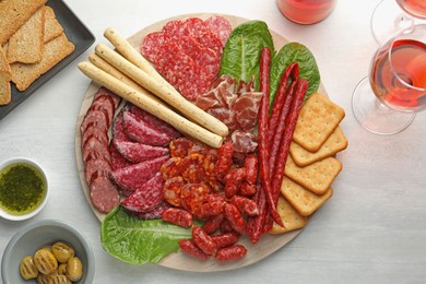 Photo of Different smoked sausages and other snacks served with wine on white table, flat lay