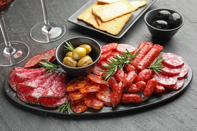 Photo of Different smoked sausages, olives, crispbreads and rosemary on black table, closeup