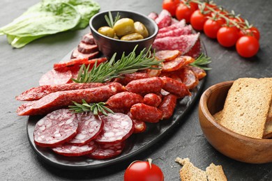 Photo of Different smoked sausages and other snacks on black table, closeup