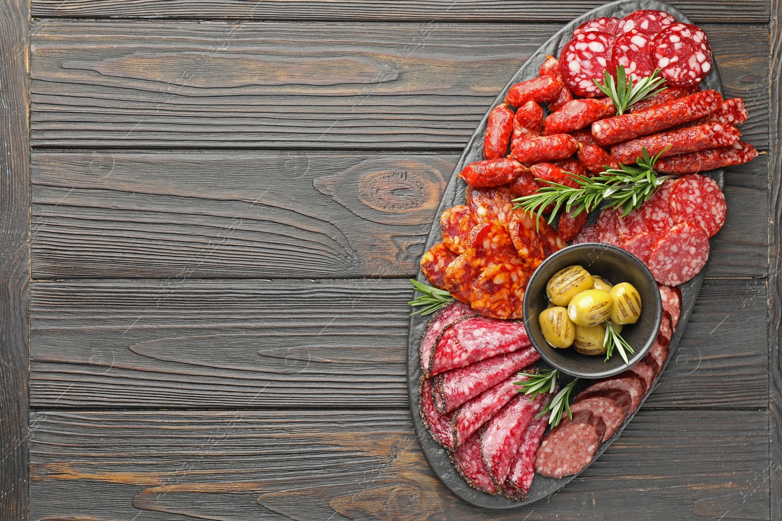 Photo of Different smoked sausages, olives and rosemary on wooden table, top view. Space for text