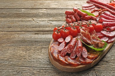 Photo of Different smoked sausages, ham and tomatoes on wooden table, closeup. Space for text