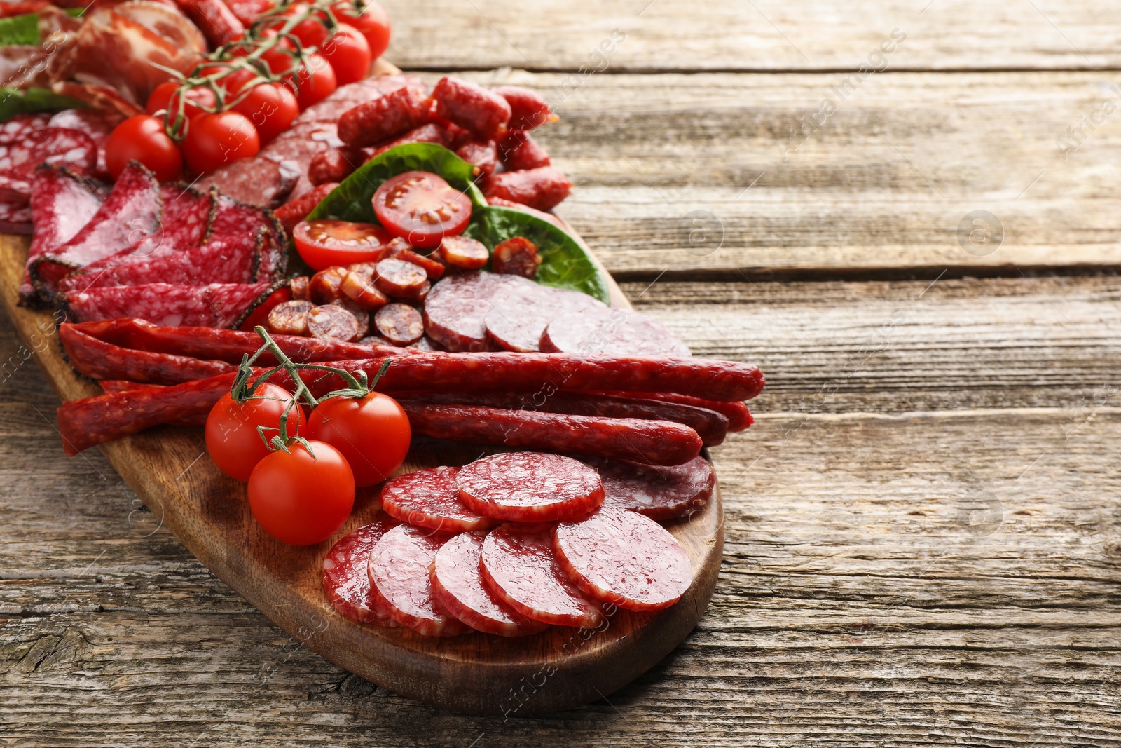 Photo of Different smoked sausages, ham and tomatoes on wooden table, closeup. Space for text