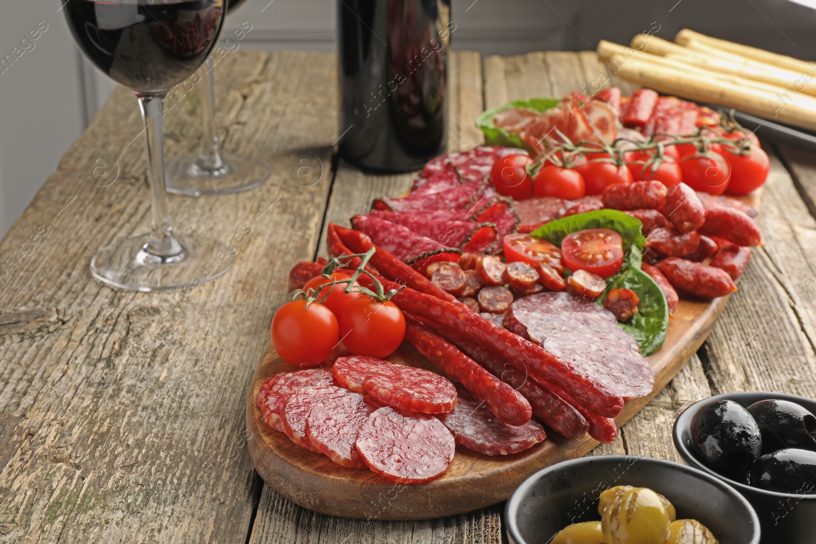 Photo of Different smoked sausages and other snacks served with wine on wooden table, closeup