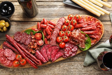 Photo of Different smoked sausages and other snacks served with wine on wooden table, flat lay