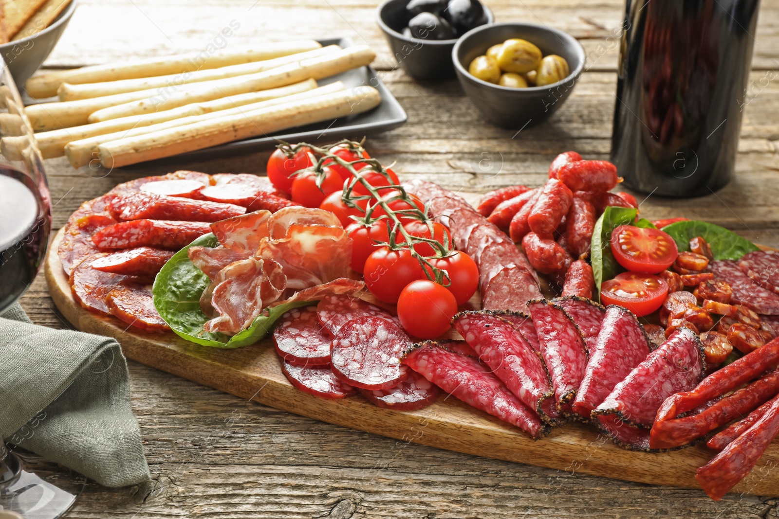 Photo of Different smoked sausages and other snacks served with wine on wooden table, closeup