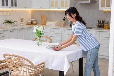 Photo of Woman putting plates on table with white tablecloth in kitchen