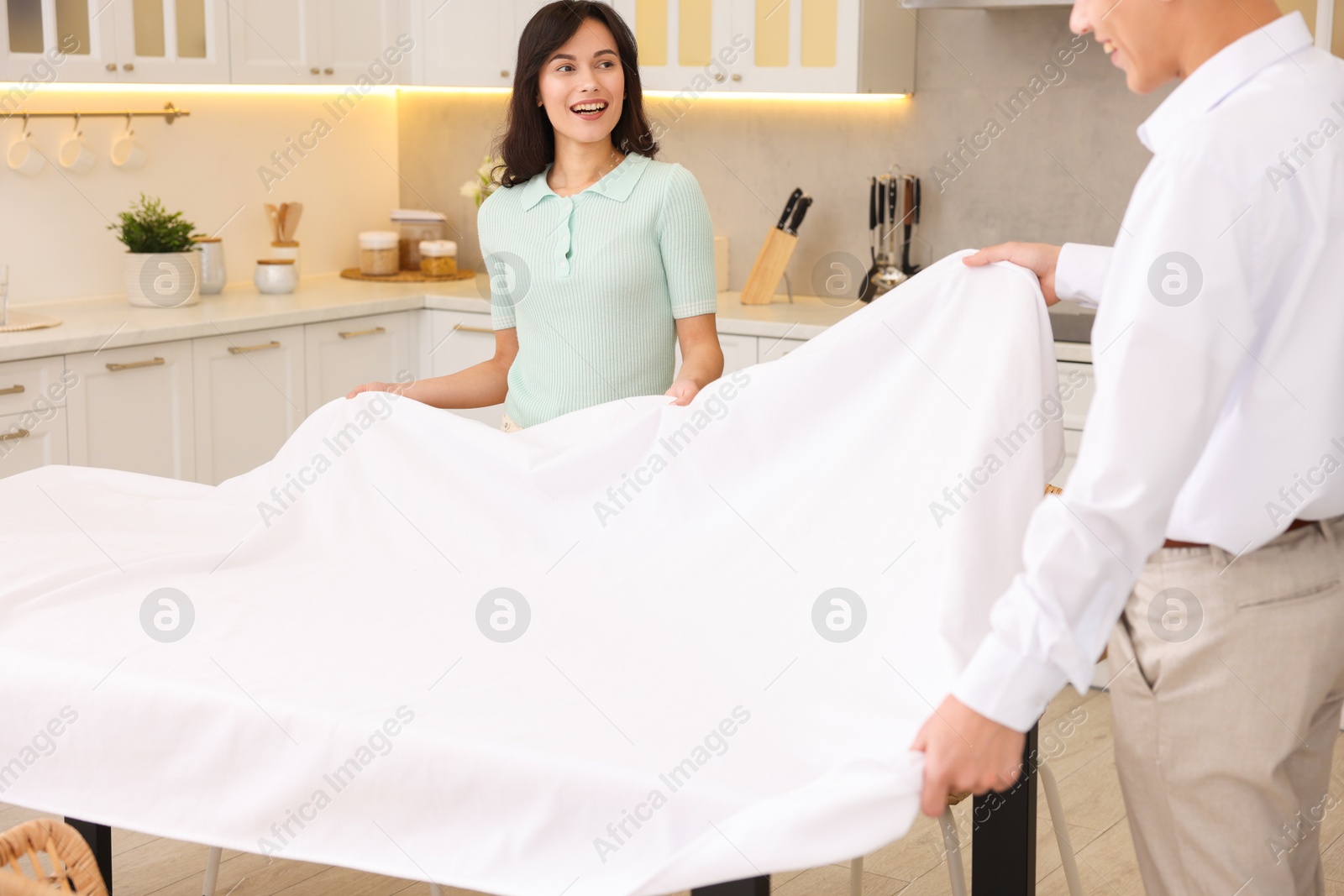 Photo of Couple putting white tablecloth on table in kitchen