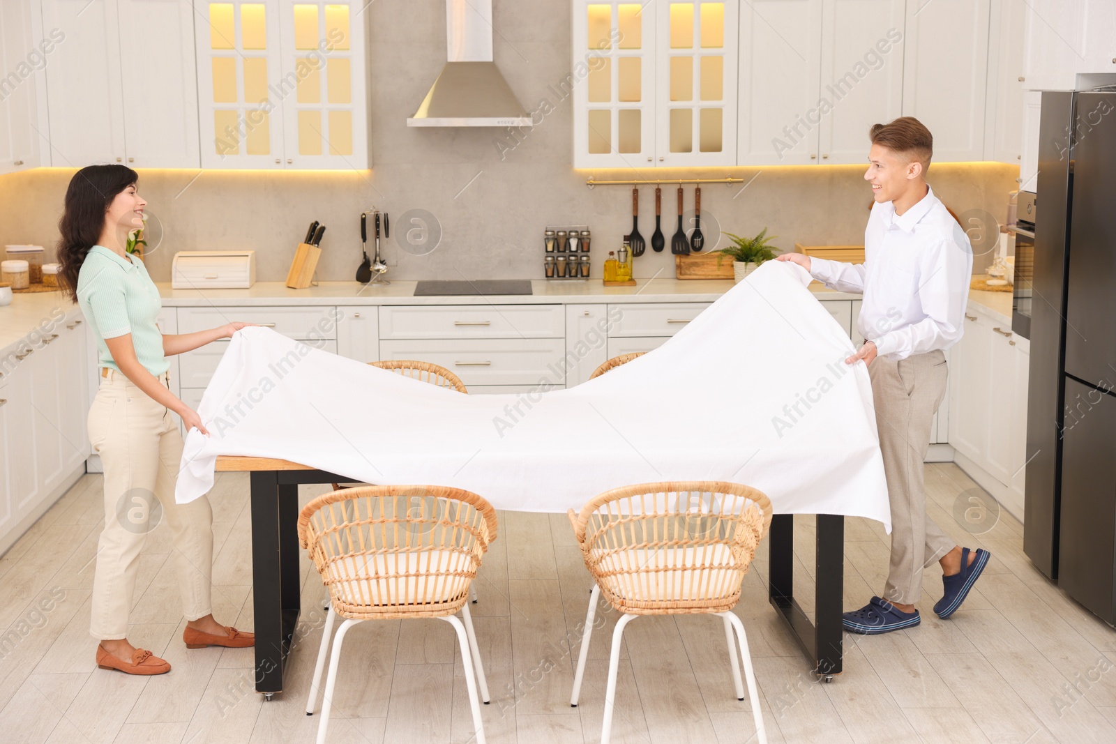 Photo of Couple putting white tablecloth on table in kitchen