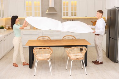 Photo of Couple putting white tablecloth on table in kitchen