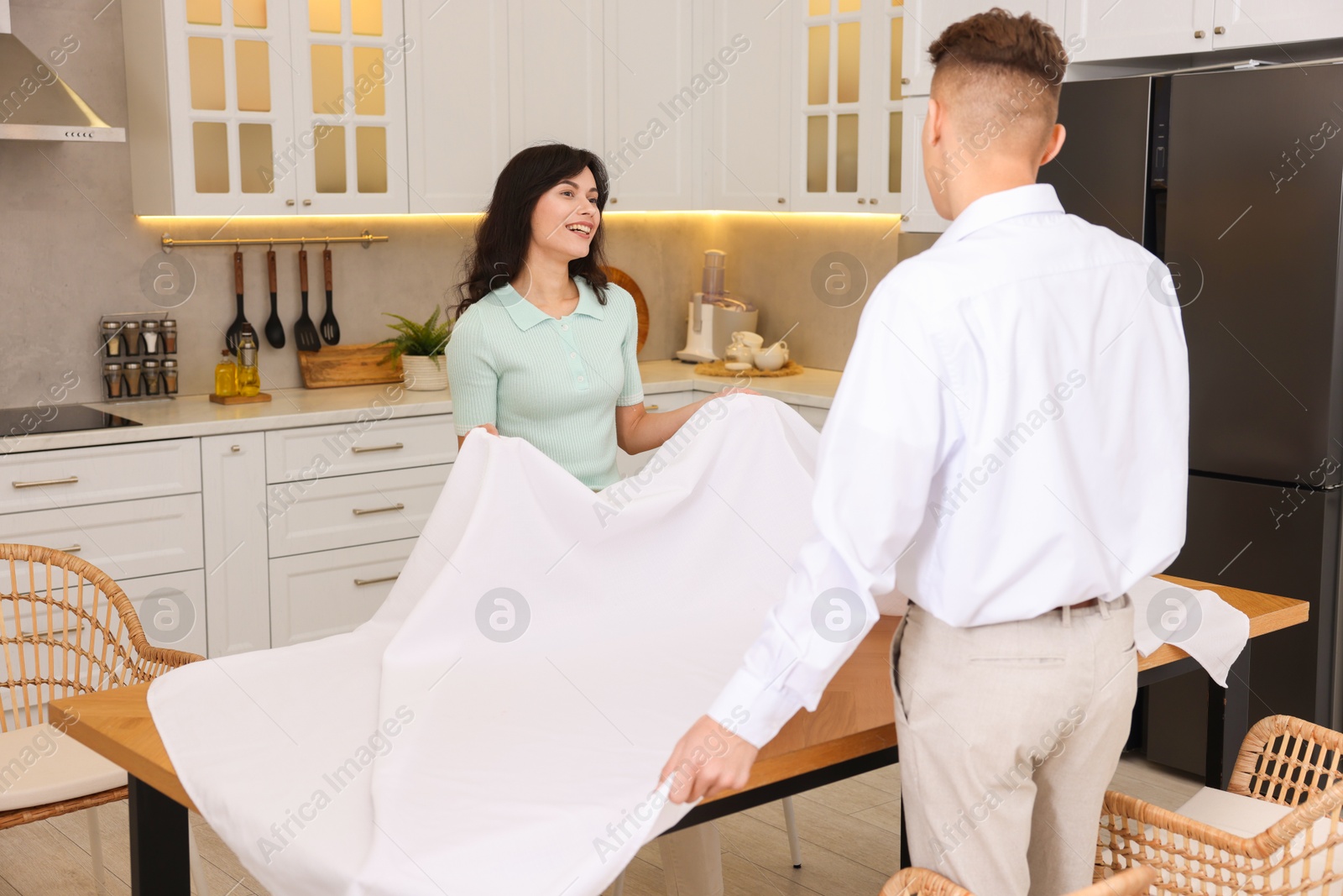 Photo of Couple putting white tablecloth on table in kitchen