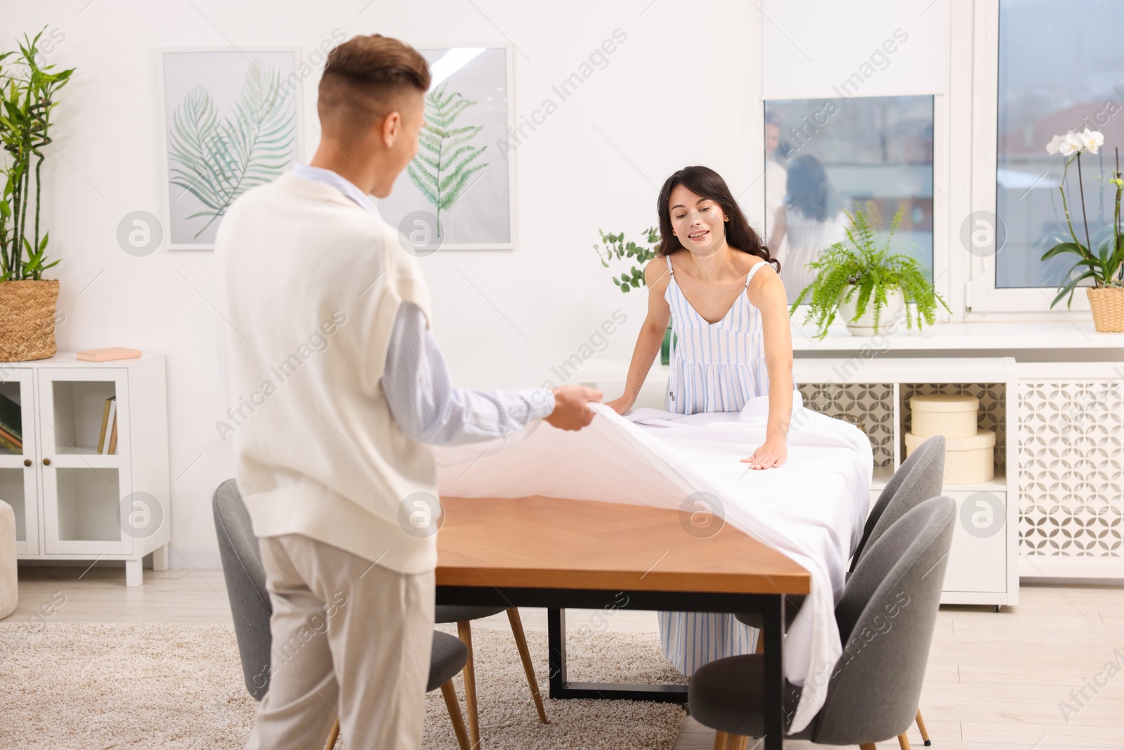 Photo of Couple putting white tablecloth on table at home