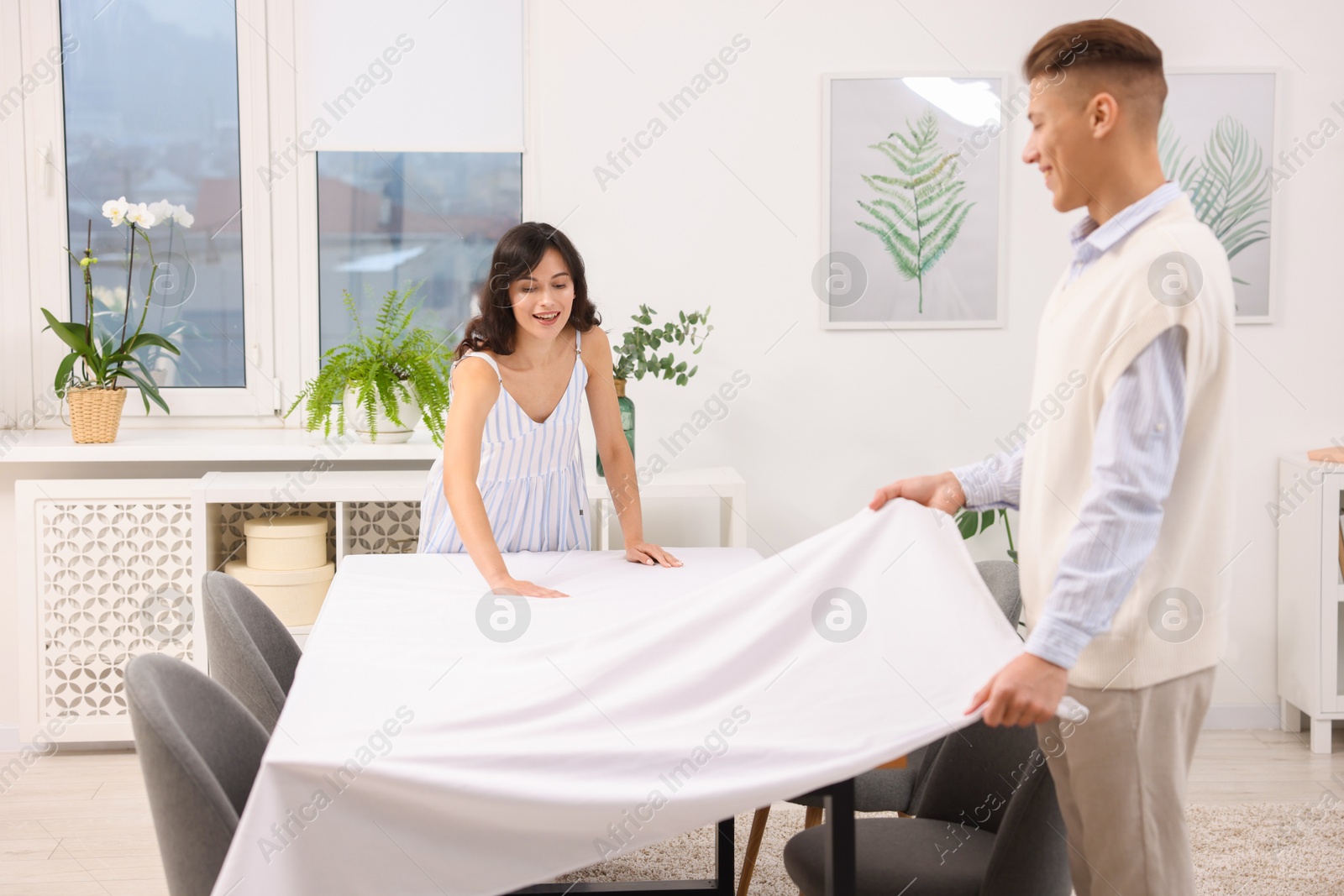 Photo of Couple putting white tablecloth on table at home