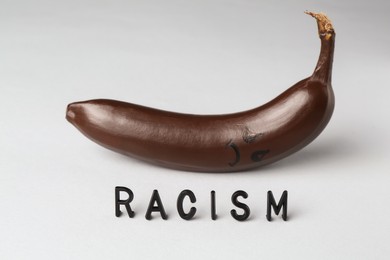 Photo of Word Racism and dark banana with sad face on light grey background