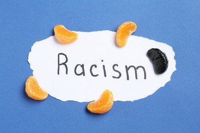 Photo of Card with word Racism and tangerine segments of different colors on blue background, top view