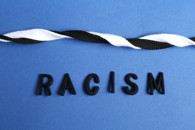 Photo of Word Racism and intertwined shoelaces of different colors on blue background, closeup