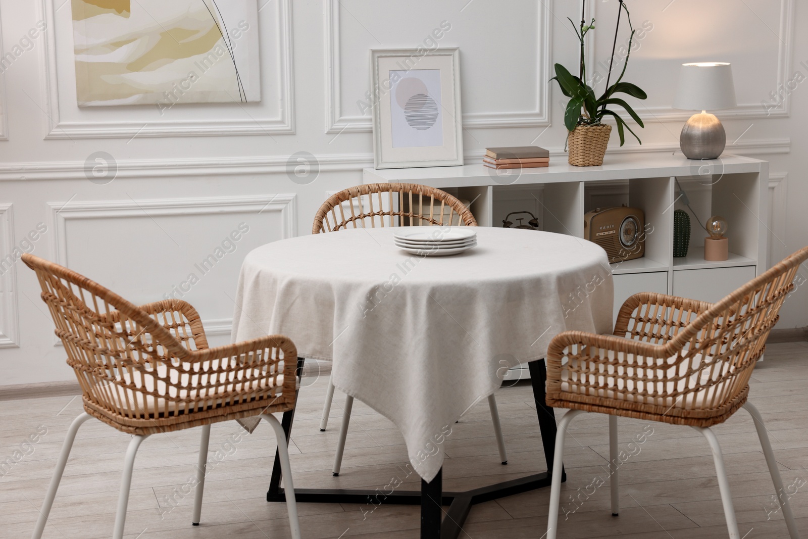 Photo of Table with white tablecloth, plates and chairs in stylish room. Interior design