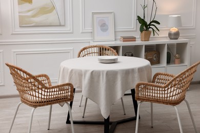 Photo of Table with white tablecloth, plates and chairs in stylish room. Interior design