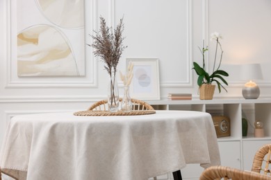 Table with white tablecloth and dried flowers in vases in stylish room. Interior design