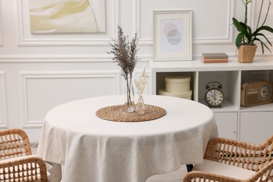 Photo of Table with white tablecloth, dried flowers in vases and chairs in stylish room. Interior design