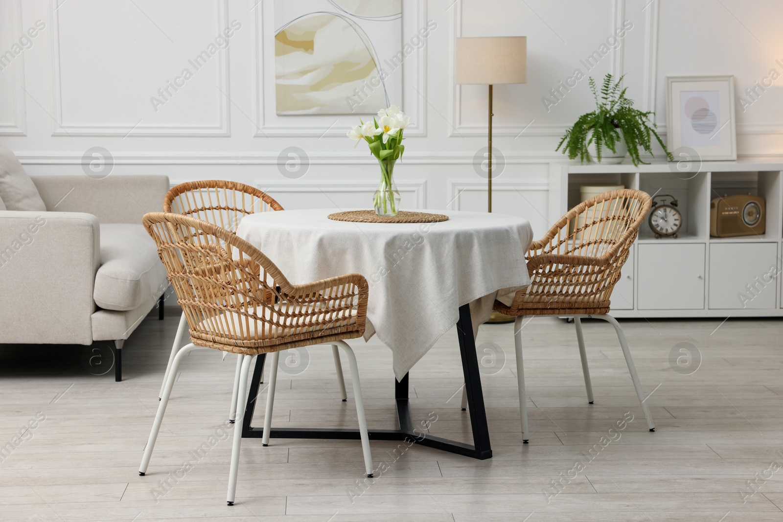 Photo of Table with white tablecloth, flowers in vase and chairs in stylish room. Interior design