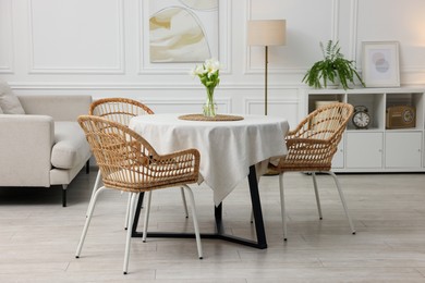 Table with white tablecloth, flowers in vase and chairs in stylish room. Interior design