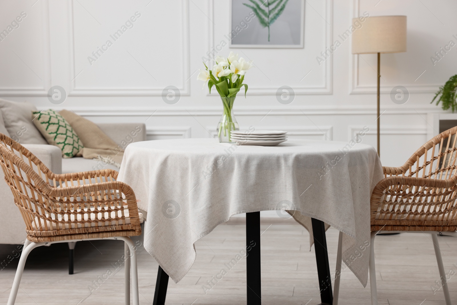 Photo of Table with white tablecloth, flowers in vase and chairs in stylish room. Interior design