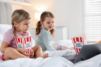 Photo of Cute little sisters with popcorn buckets watching something on laptop at home, selective focus