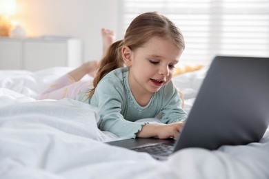 Photo of Cute little girl using laptop on bed at home