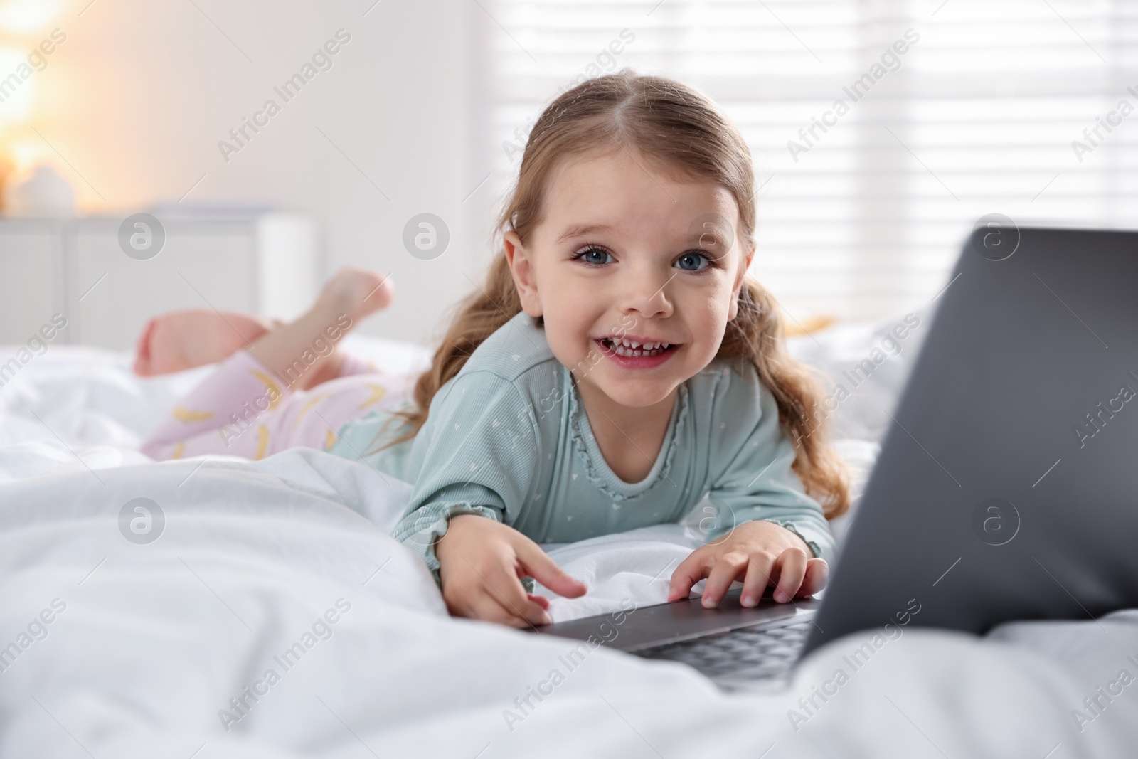 Photo of Cute little girl using laptop on bed at home